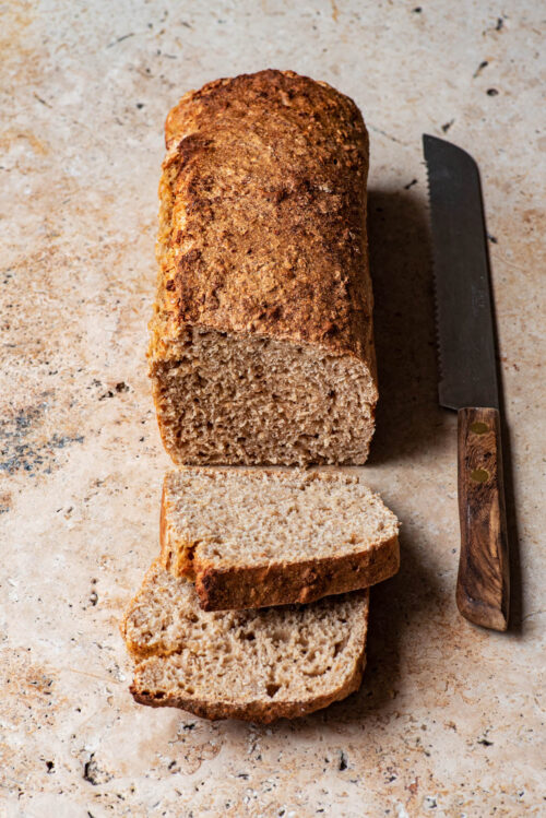 A loaf of bread with two slices cut and a knife alongside.