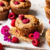 Several muffins with raspberries and pink bachelor's buttons around.