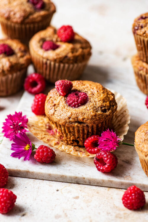 Several muffins with raspberries and pink bachelor's buttons around.