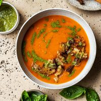 A bowl of tomato soup with rough croutons and pesto added.