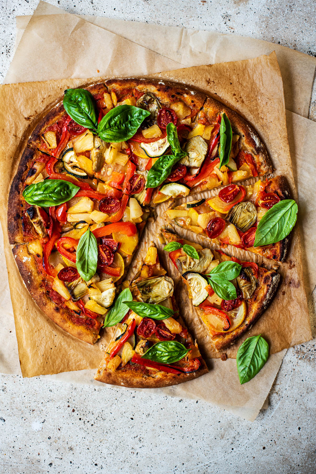 Top down view of pizza topped with vegetables and fresh basil.