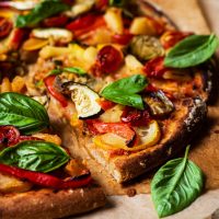 Vegetable topped pizza cut into triangles, side view.