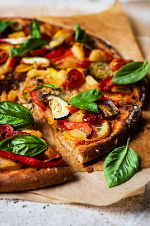 Vegetable topped pizza cut into triangles, side view.