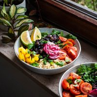 Two burrito bowls on a window ledge with a small plant in background.