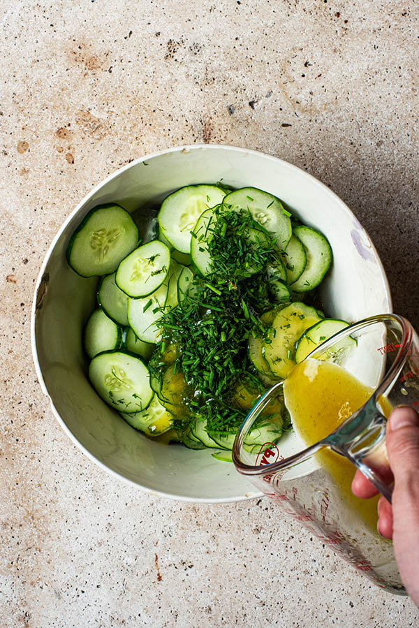 Pouring the vinaigrette over the cucumbers.