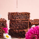 Chocolate drizzling onto a stack of three brownies.