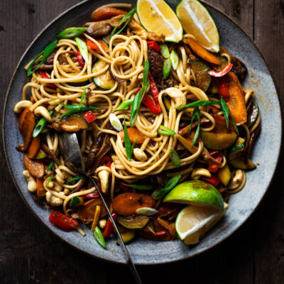 Vegetable soba noodle stir fry in a large bowl with lime wedges.