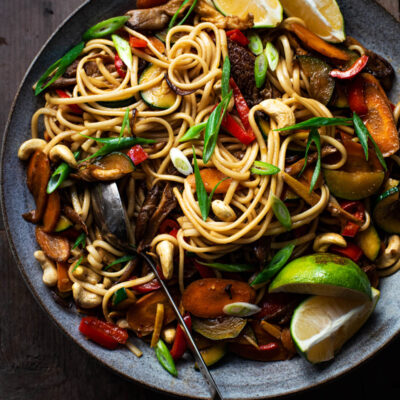 Close up of a stir fry noodle bowl with lime wedges.