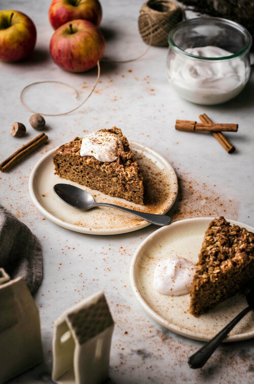 Two slices of apple crumble cake on small plates with yogurt.