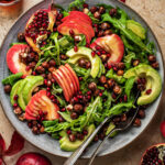 Large salad with sliced apples, avocado, nuts, and pomegranate.