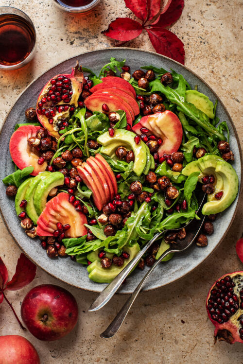 Large salad with sliced apples, avocado, nuts, and pomegranate.