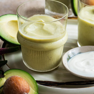 Close up of avocado milkshake in three glasses with avocados around.