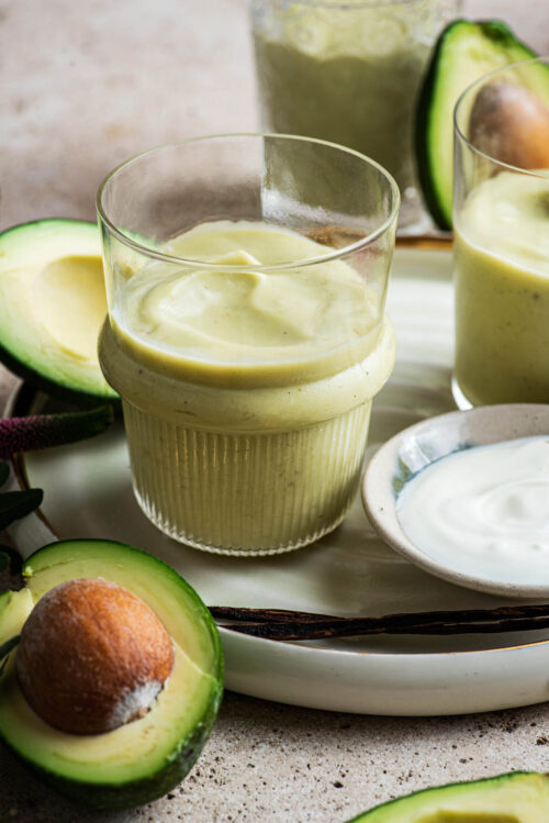 Close up of avocado milkshake in three glasses with avocados around.