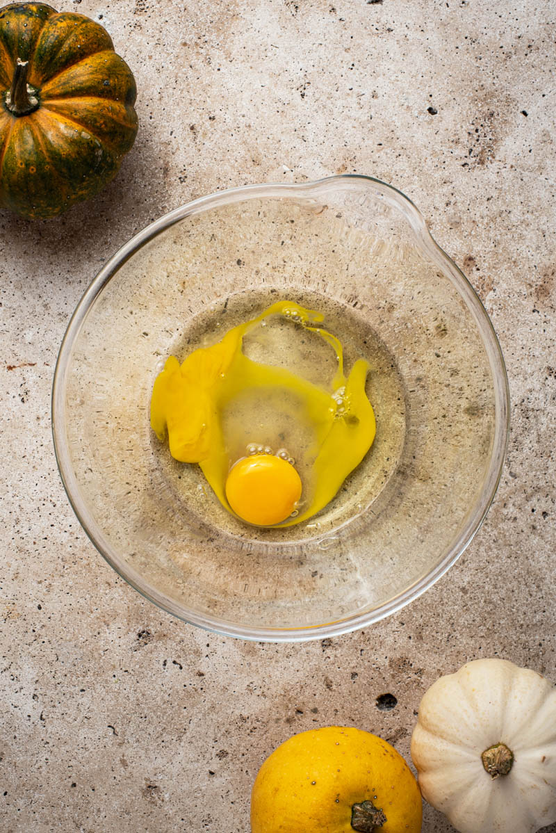 Two eggs added to a large glass mixing bowl.