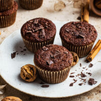 Three muffins on a plate with more around, chocolate, and nuts.