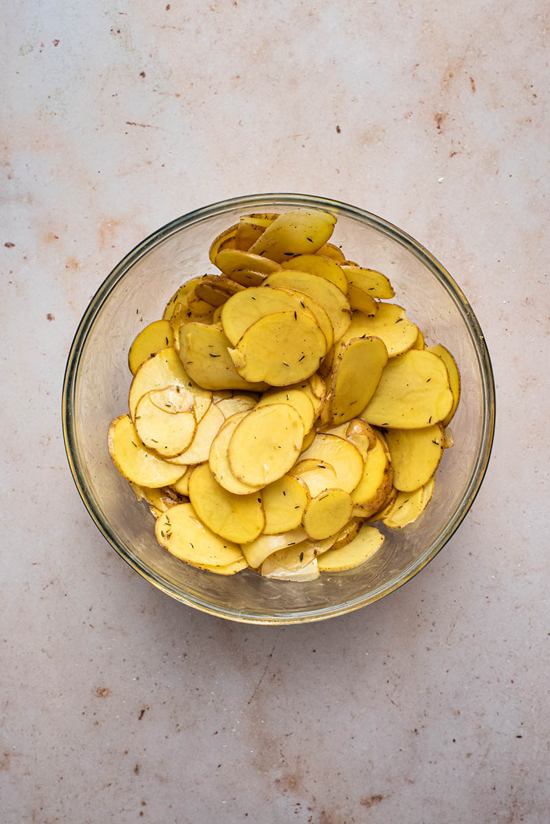 Thinly sliced potatoes mixed with spices and oil in a bowl.