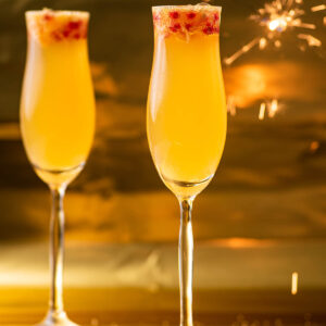 Two glasses of an orange mocktail with a sparkler in the background.