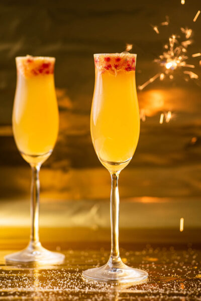 Two glasses of an orange mocktail with a sparkler in the background.
