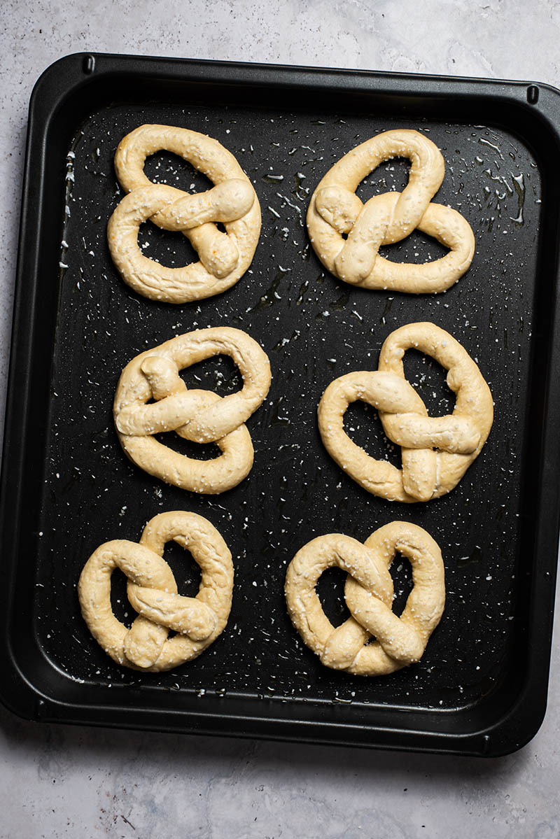 Six pretzels on a baking sheet after being boiled.