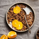 A shallow bowl of granola with orange slices and oat milk.