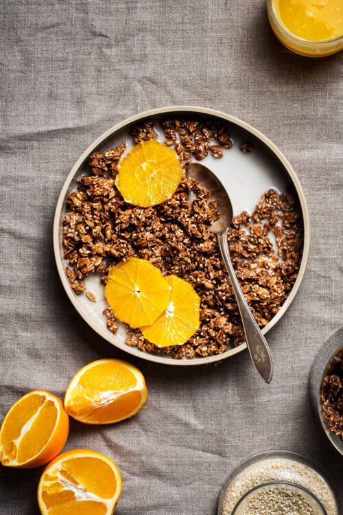 A shallow bowl of granola with orange slices and oat milk.
