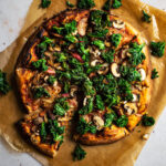 Kale topped pizza on two sheets of parchment paper.