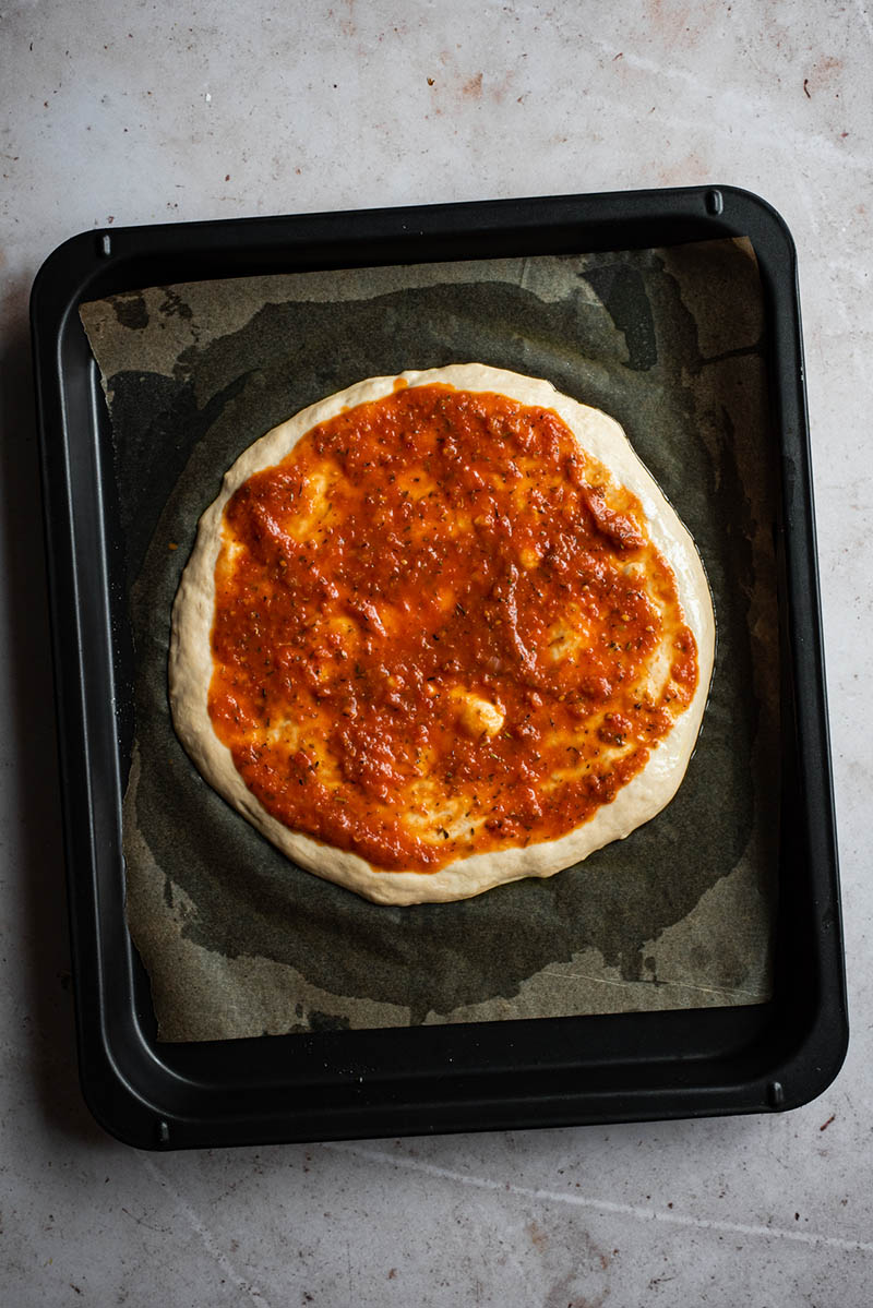Pizza dough topped with tomato sauce.