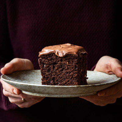 Woman holding a plate with a piece of ganache topped chocolate cake.