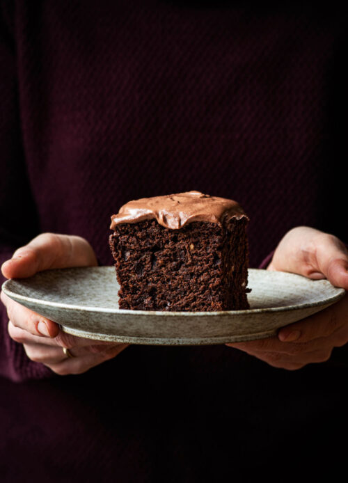Woman holding a plate with a piece of ganache topped chocolate cake.