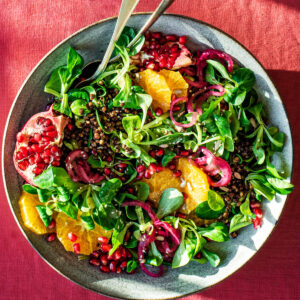 A large bowl of salad with lentils, orange and pomegranate.