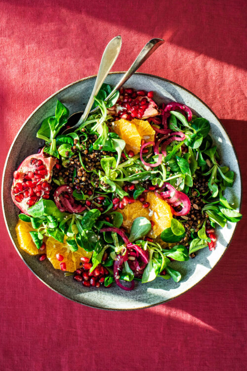 A large bowl of salad with lentils, orange and pomegranate.