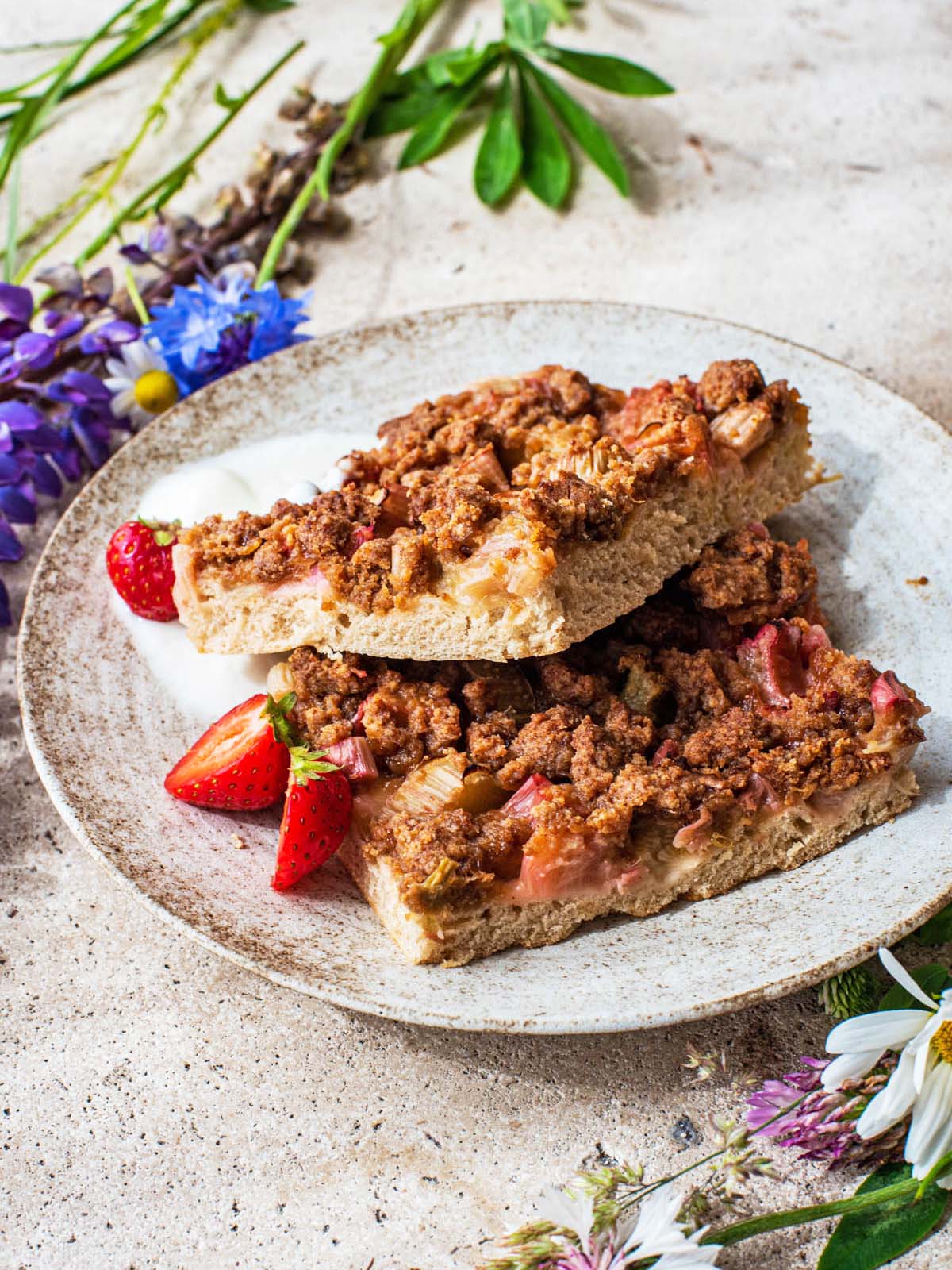 Two pieces of cake on a plate with wildflowers around.