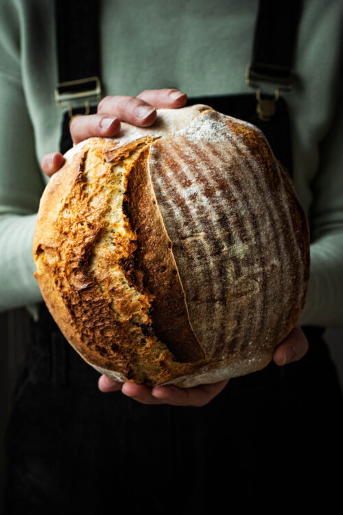 Woman holding a loaf of bread in front of her.
