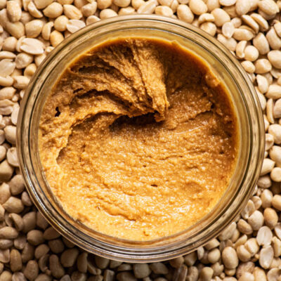 Top down view of a jar of peanut butter with a peanut background.