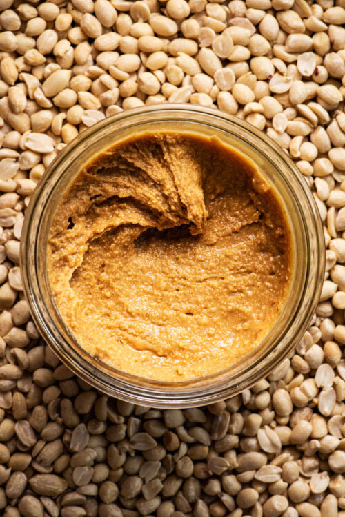 Top down view of a jar of peanut butter with a peanut background.