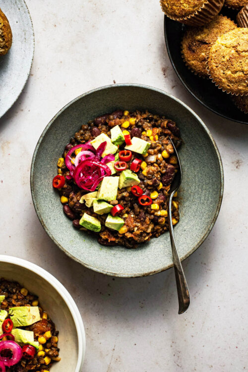 Chili in a shallow bowl with avocado and pickled red onion.