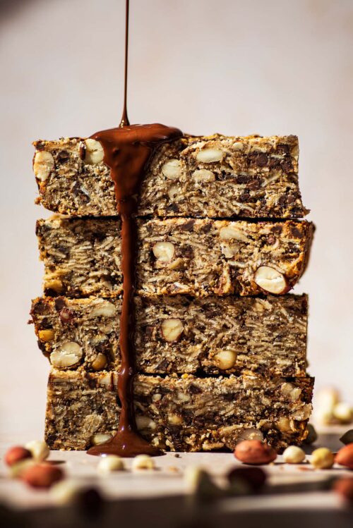 A stack of four granola bars with chocolate being drizzled on them.