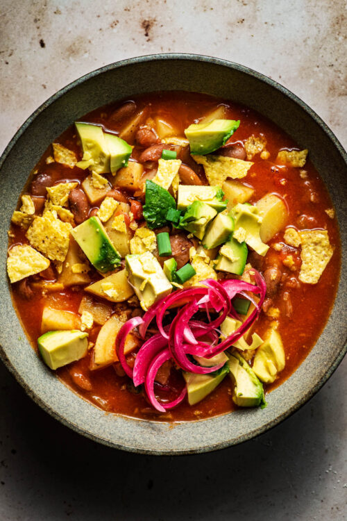 Pinto bean soup with tortilla chips, avocado, and red onion.