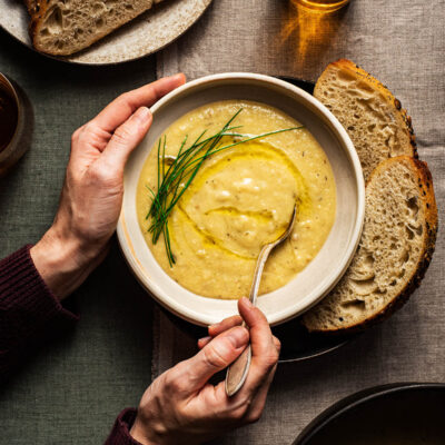 A bowl of creamy parsnip soup with bread and herbs.