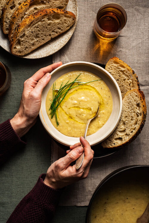 A bowl of creamy parsnip soup with bread and herbs.