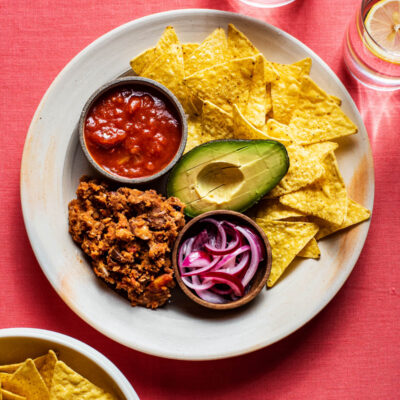 Refried beans on a place with tortilla chips, avocado, and salsa.