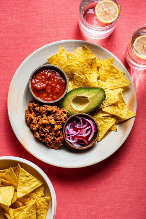Refried beans on a place with tortilla chips, avocado, and salsa.