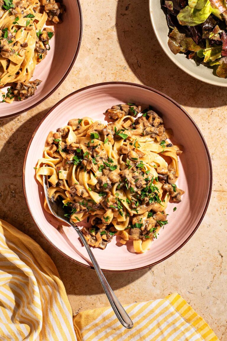 Pasta with mushroom sauce on two plates with salad beside.
