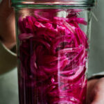 Woman holding a large jar of pickled red onions with a lid.