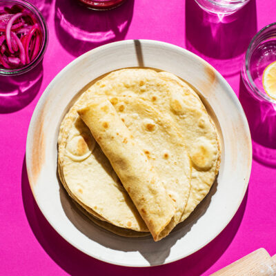A stack of tortillas on a plate, with one rolled.
