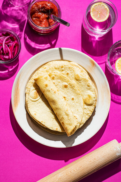 A stack of tortillas on a plate, with one rolled.