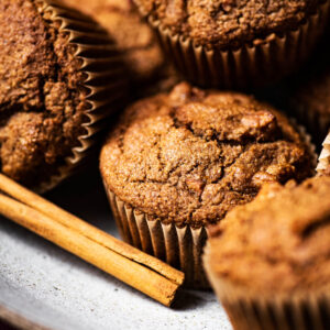 Several muffins piled in a shallow bowl with a cinnamon stick.