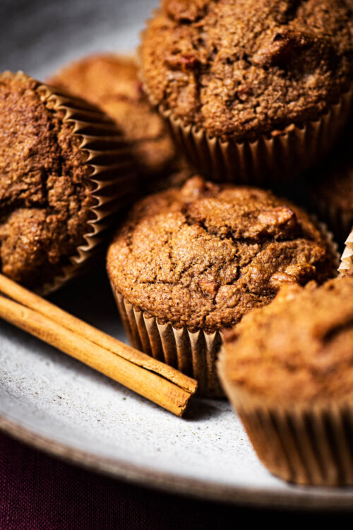 Several muffins piled in a shallow bowl with a cinnamon stick.