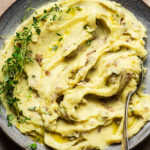 A bowl of creamy mashed potatoes with thyme.