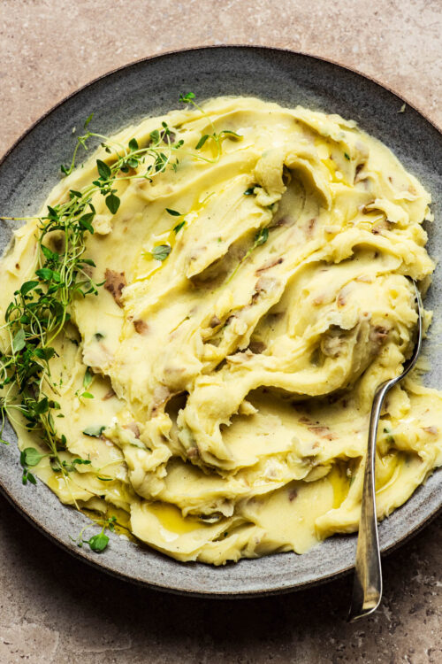 A bowl of creamy mashed potatoes with thyme.